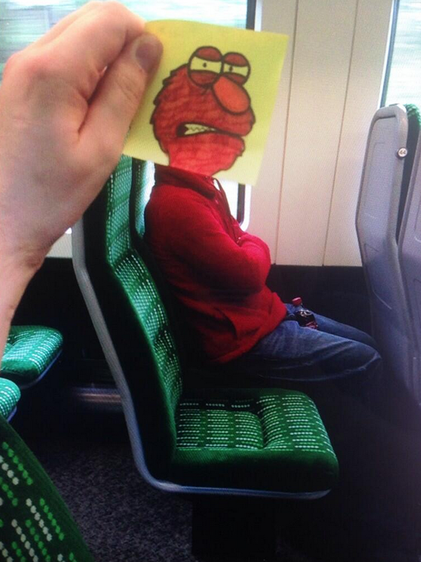 Funny sketch of Tickle Me Elmo's head against a real-life person on the train with arms folded.