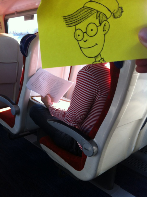 Funny sketch of Wally's head put on a guy wearing a red and white striped shirt on the commute to work looking at an essay.