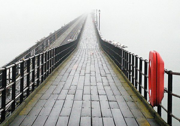 Moody photograph of a pier disappearing into grey mist