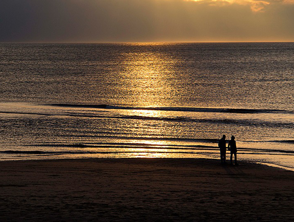 Golden sunset over the sea as a silhouetted couple walk along the shore on the beach