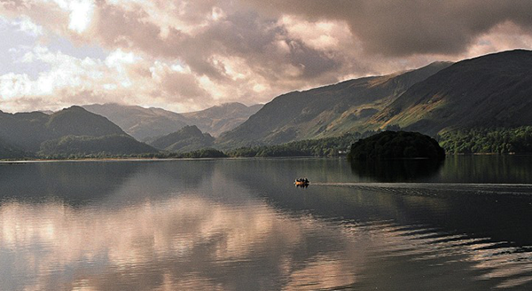Stunning photographic image of a stormy lake and valley backdrop with a tiny boat on the otherwise still, calm water