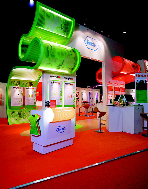 Quirky Roche exhibition stand has red carpeting, red high chairs and a green banner